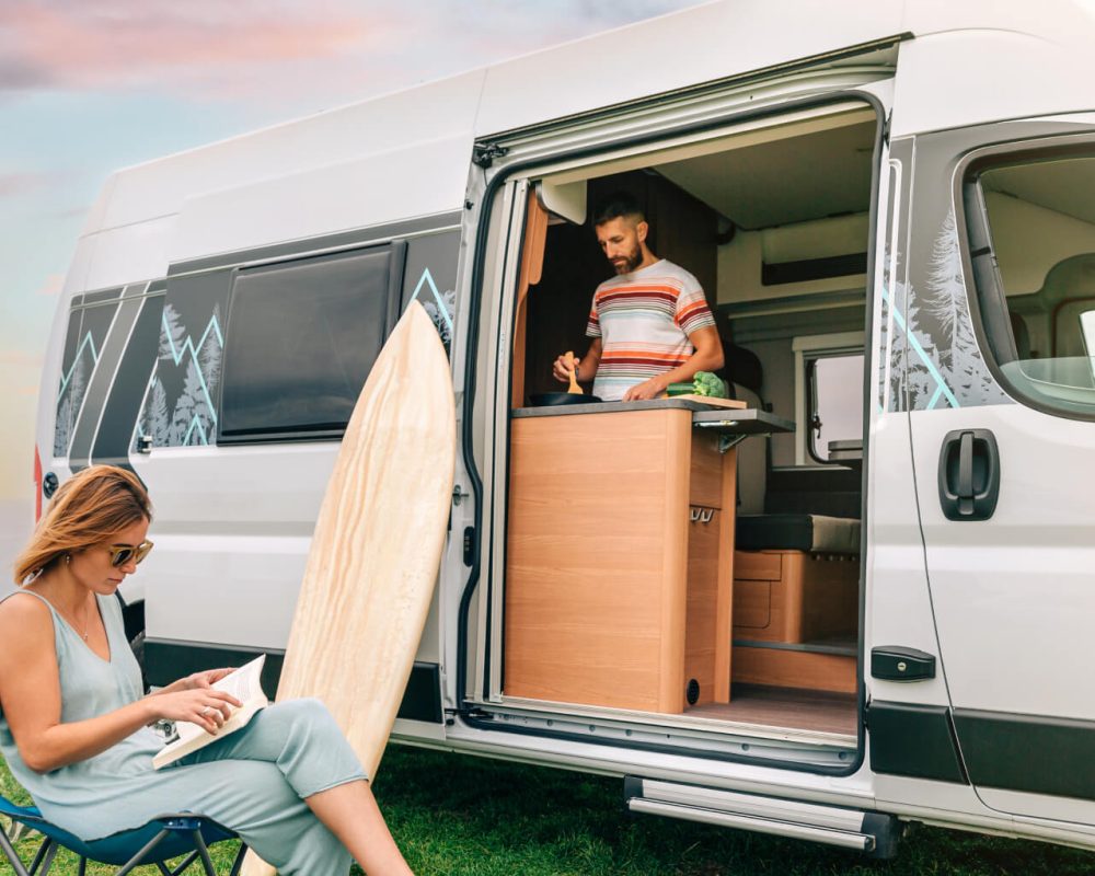 man-cooking-vegetables-in-a-camper-van-while-woman-FA8Q2L6.jpg